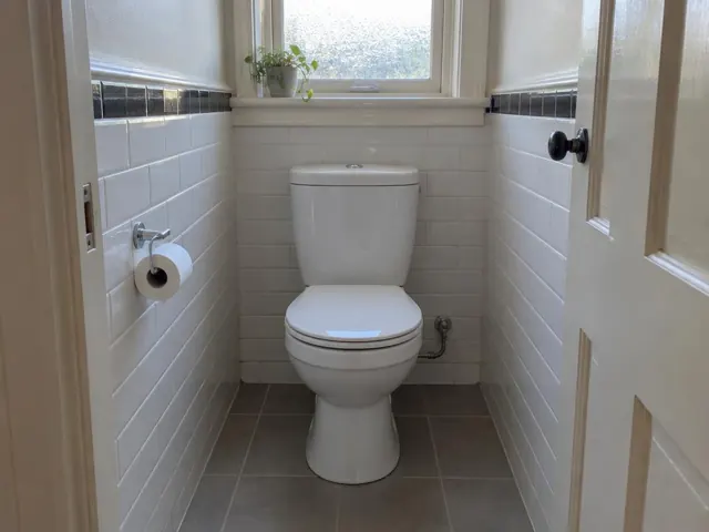 White toilet in a tiled bathroom with a frosted window and grey floor tiles in Bronte